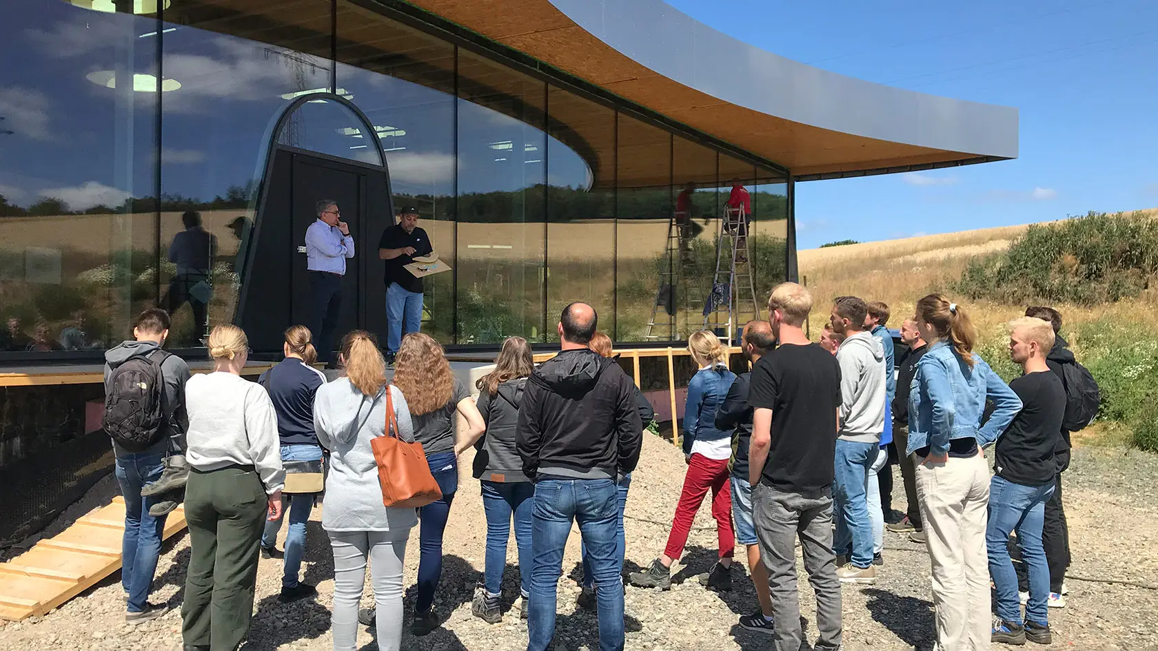 Baustellenbesuch der THM Gießen bei THE SPACE in Solms-Mittelbiel mit Gruppe vor der Glasfassade der Ausstellungshalle.