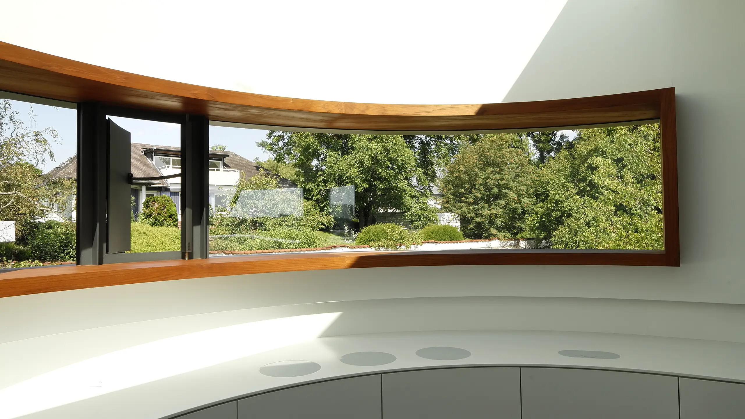 Gebogene Küche im Wohnhaus An Steins Garten in Gießen mit weißer Corian-Arbeitsfläche, runden Kochzonen und Fensterband mit Teakrahmen.