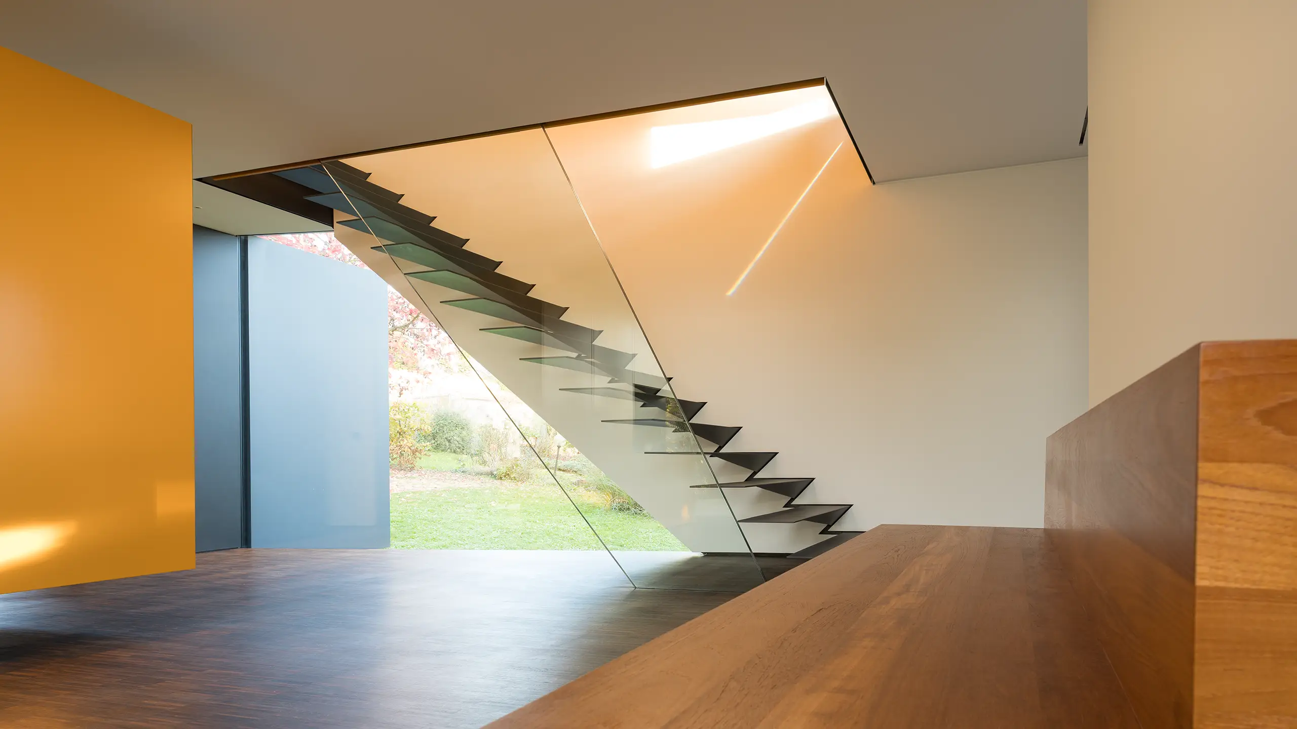 Stahltreppe mit Kragstufen im Wohnhaus An Steins Garten in Gießen, davor eine schwebende Sitzbank aus Teak.